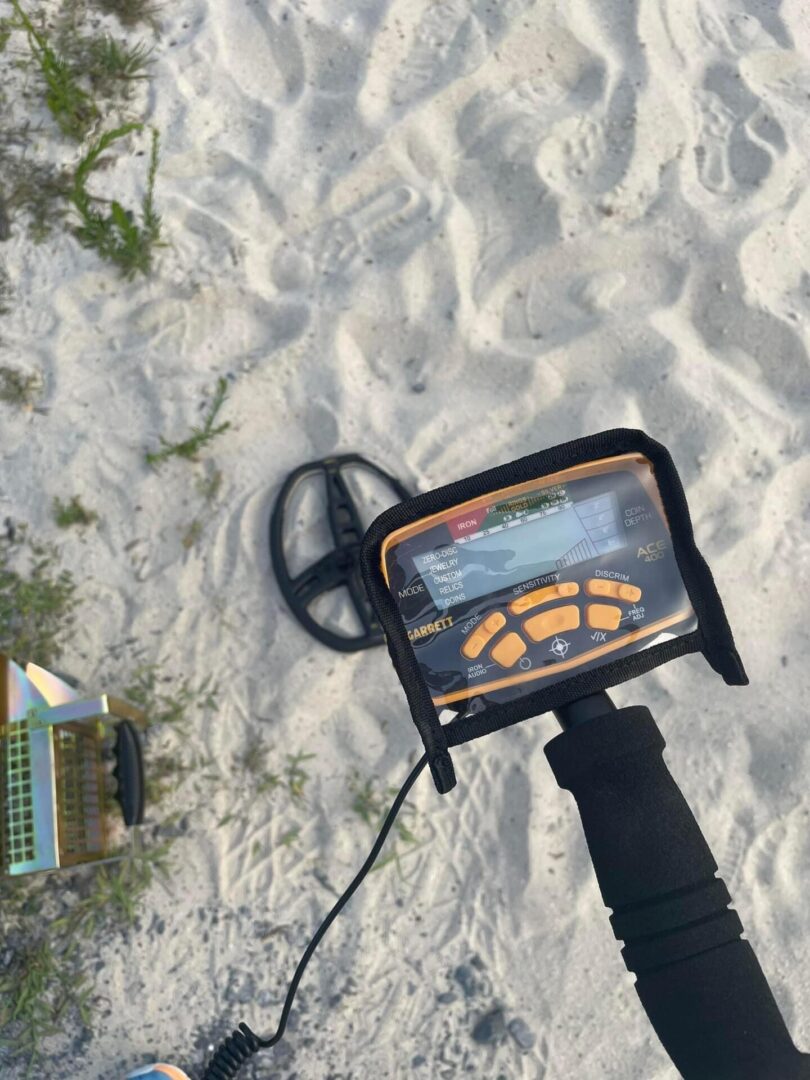 A metal detector is on the sand near some buildings.