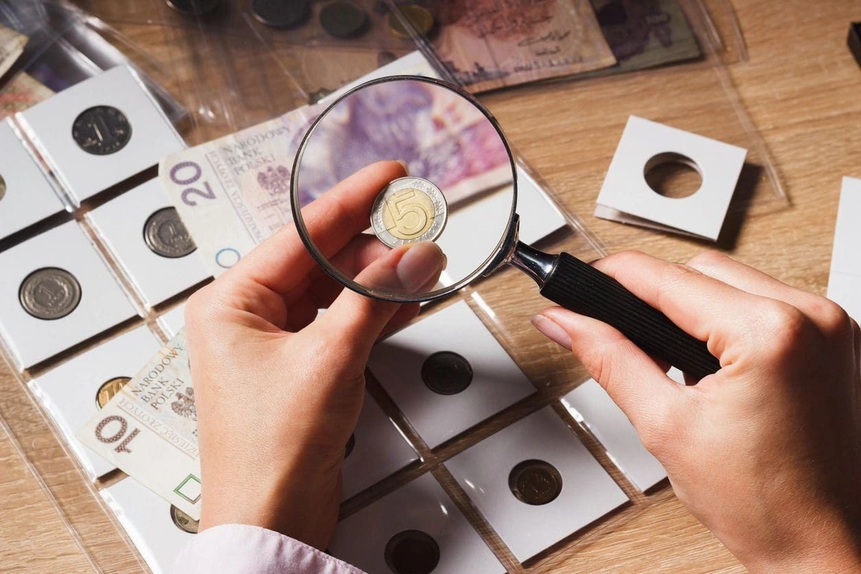A person looking at coins through a magnifying glass.